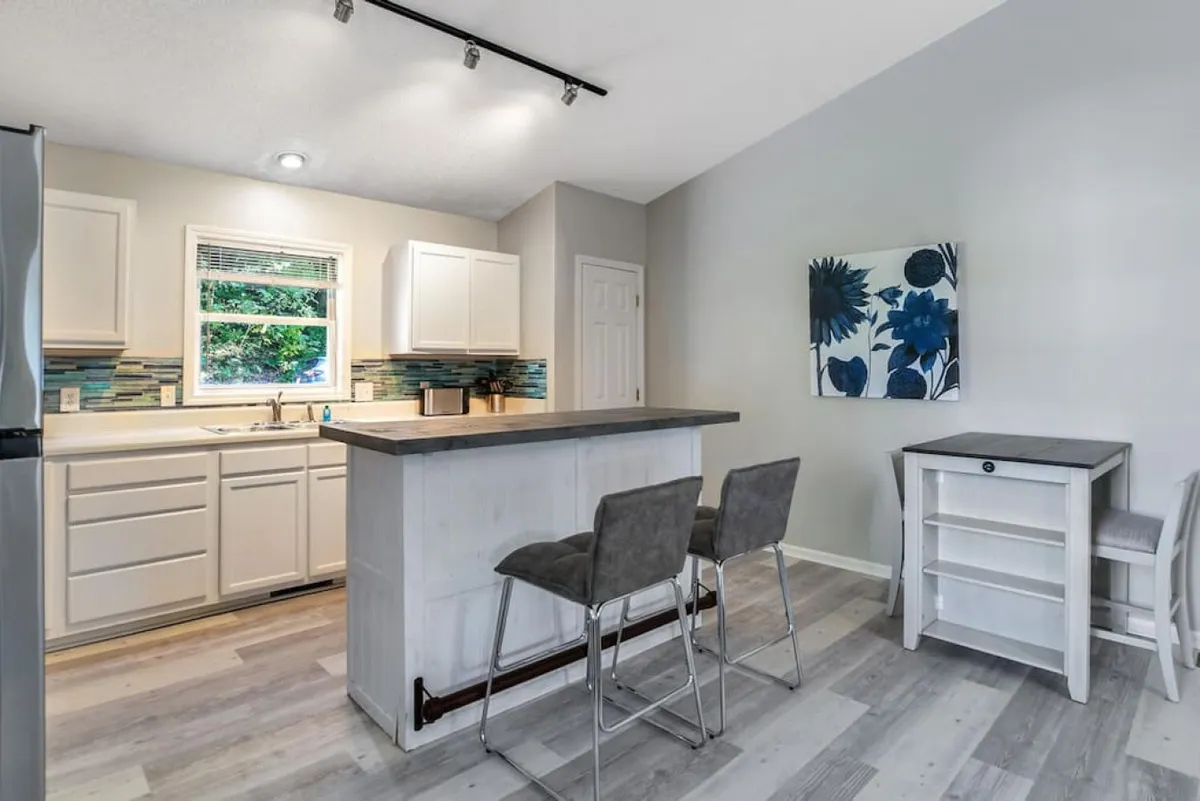 The kitchen island takes center stage in this cozy, modern kitchen accented by a colorful backsplash and vibrant wall art. Stainless steel appliances and comfortable seating invite both casual dining and entertaining, while the proximity to the dining area is evident, supporting lively gatherings and family connections.