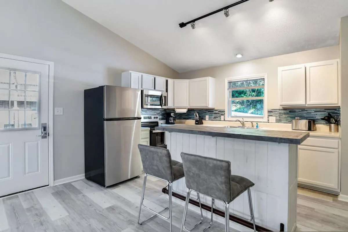 This image showcases a spacious, open-concept kitchen featuring a central island, gleaming stainless steel appliances, and crisp white cabinetry. The scene hints at lively cooking sessions and shared meals, with natural light creating a bright and welcoming ambiance. The island offers ample room for meal prep, casual dining, or friendly conversation.