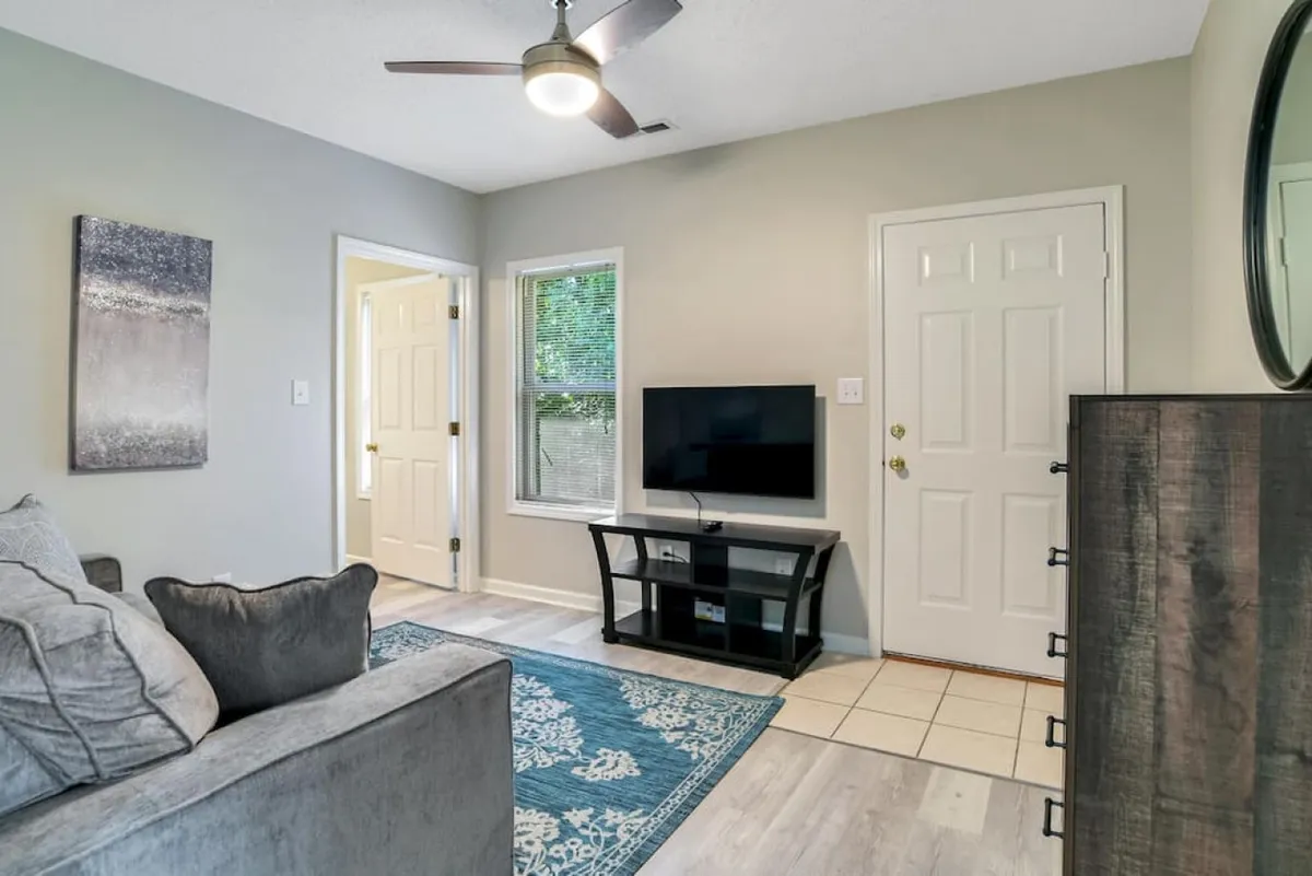 A cozy and modern living space with a plush sofa, vibrant area rug, wall art, a television, and an entrance door. The layout encourages conversation, lounging, or movie nights with family and friends.