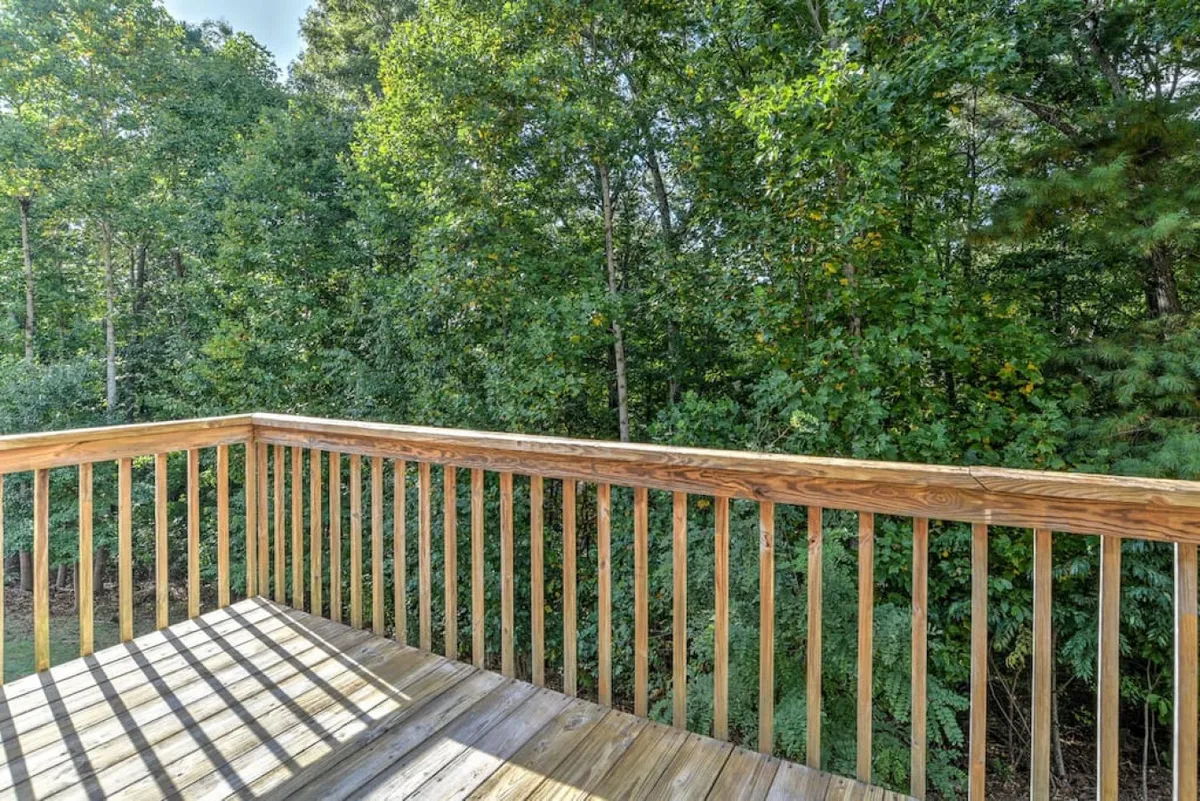 A tranquil outdoor deck with a wooden railing overlooks a lush green landscape, inviting guests to relax, enjoy nature, or socialize. The space appears roomy enough for both people and pets to stretch out and savor the outdoors.