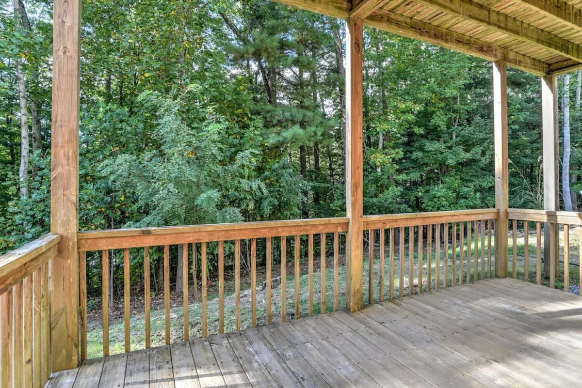 Another exterior deck scene, featuring a wooden railing and expansive views of surrounding trees. The deck flooring and leafy canopy create a comfortable, inviting spot for nature watching or enjoying the outdoors with a furry companion.